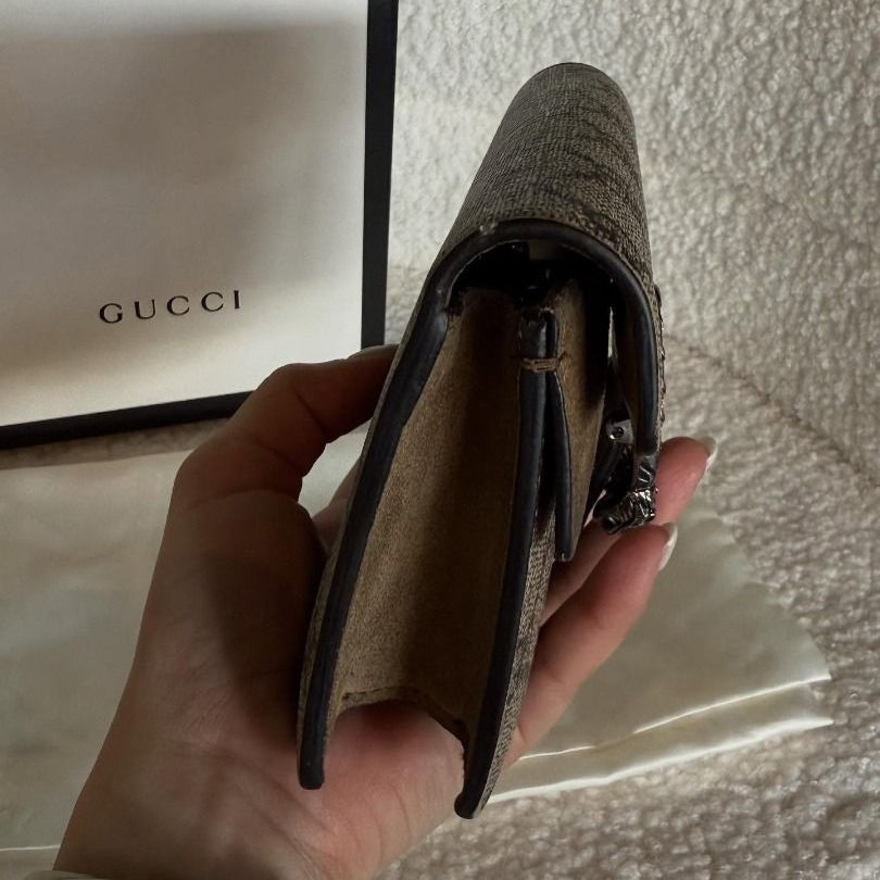 Hand holding a textured wallet with a Gucci bag in the background