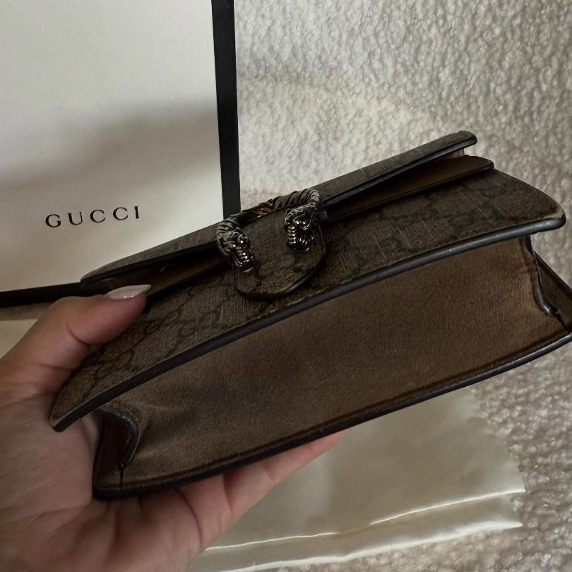 Brown Gucci clutch held by a hand with a Gucci box in the background.